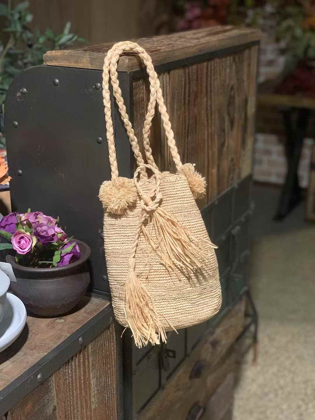 drawstring raffia bucket bag in earth tone beige color with pom pom on the top of edge