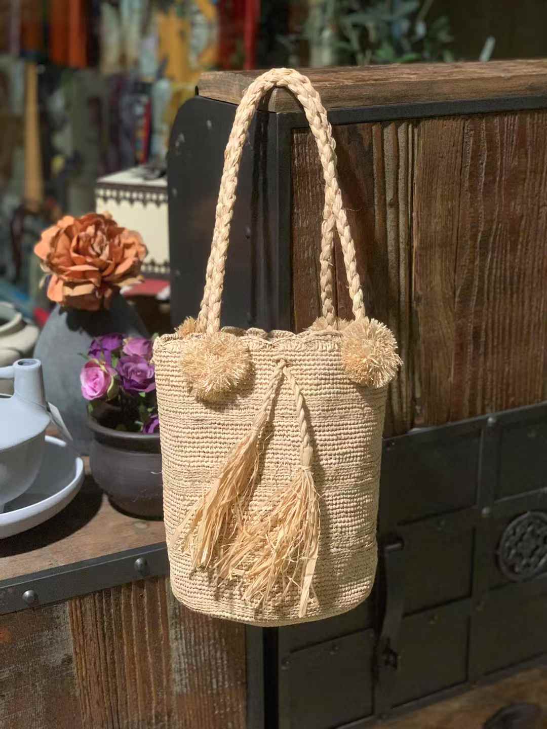 raffia bucket bag in earth tone beige color with pom pom on the top of edge, 2 woven handles
