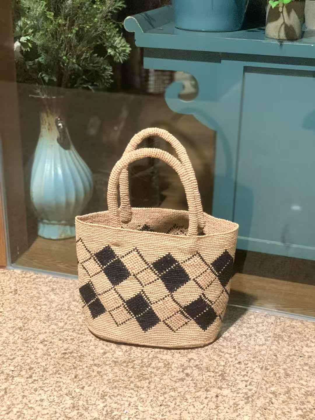 summer handbag adorned with a striking black diamond checkerboard pattern on a natural raffia base.