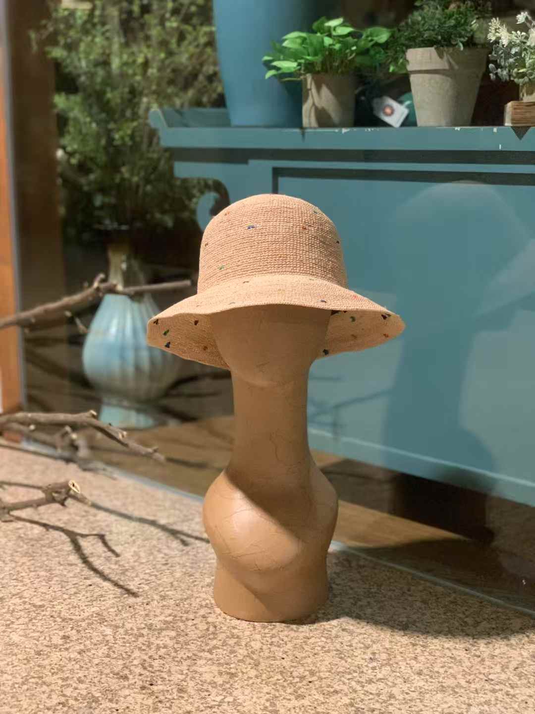 Natural beige raffia straw hat with wide brim and colorful speckles, hand-crocheted sun hat displayed on mannequin in rustic setting