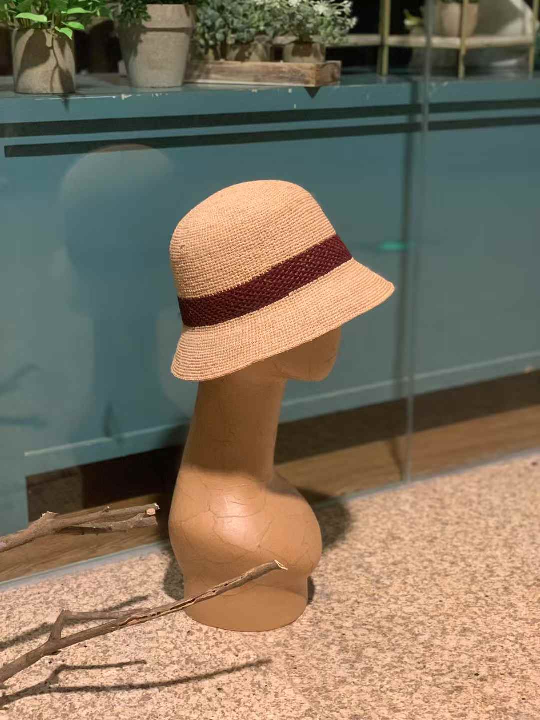 a Hand crocheted raffia bucket hat with short brim and red wine accent on a mannequin, Japanese minimalist style, lightweight summer accessory