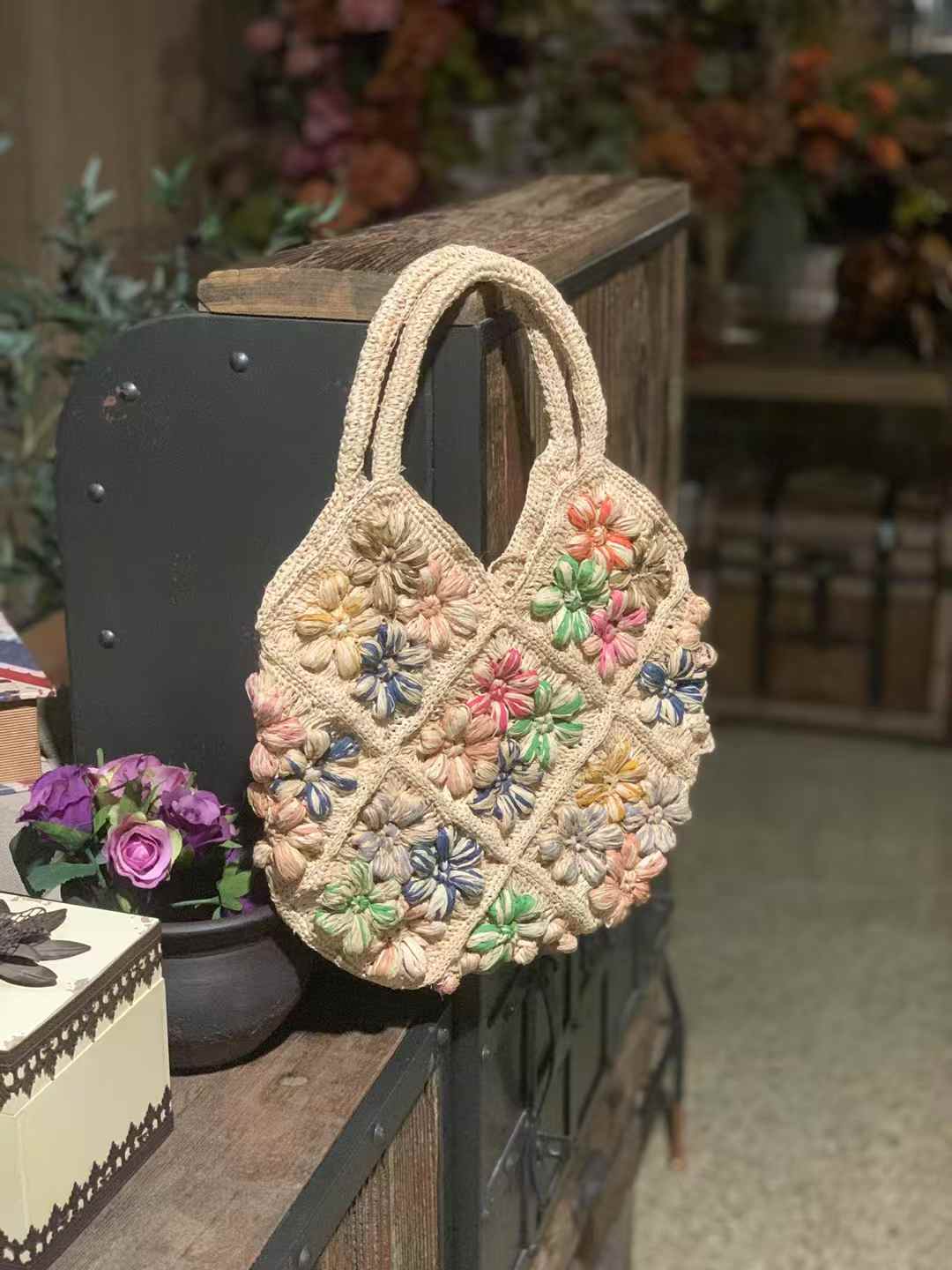 Colorful puff flowers straw bag made in crochet technique, diamond shape granny squares patch design, featuring natural tones base, two top handles — perfect for summer beach or casual wear