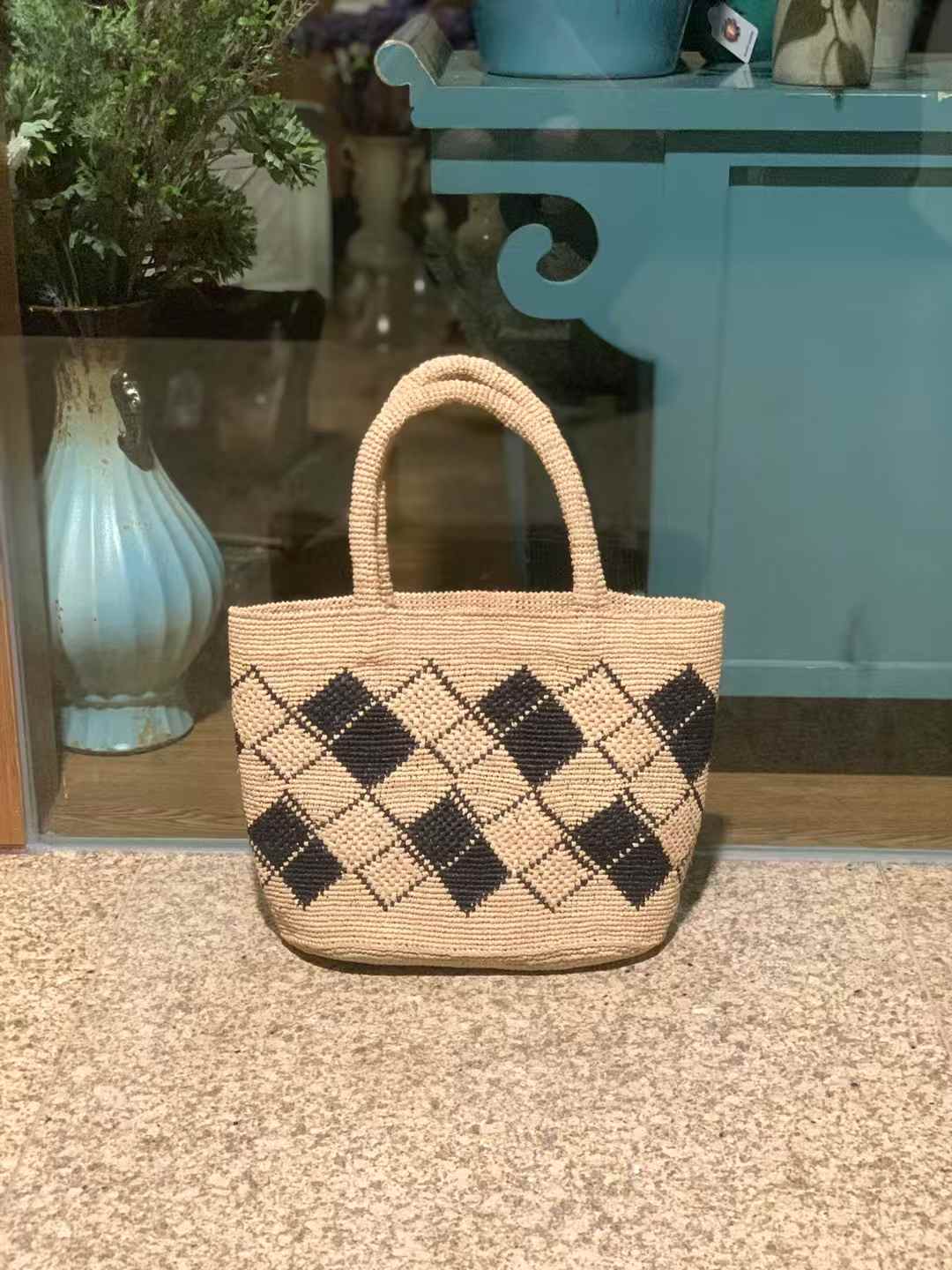 beach straw bag adorned with a geometric black diamond checkerboard pattern on a natural raffia base