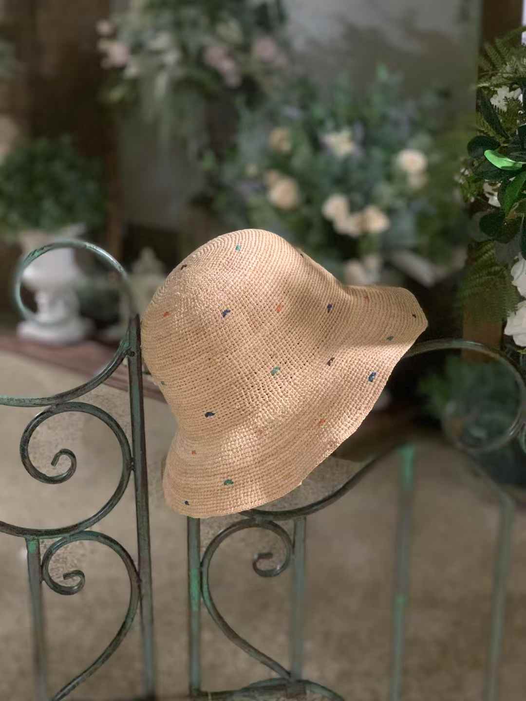 Beige color raffia bucket hat with colorful speckles all around, crocheted sun hat for women displayed on metal fence