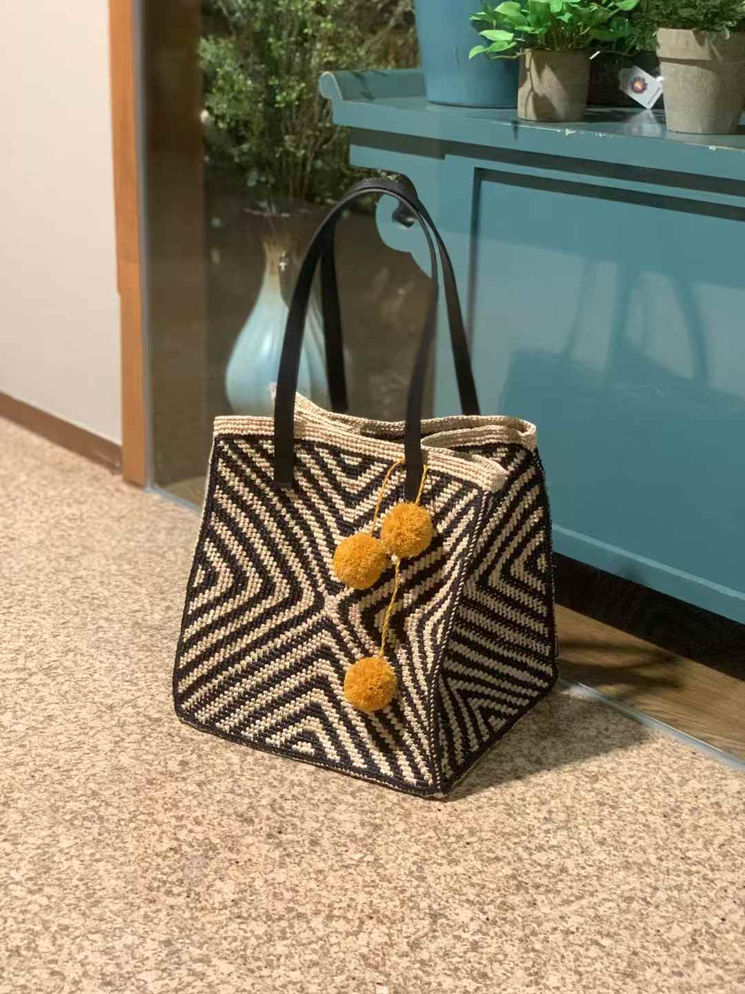 Side view of square raffia tote with bold chevron pattern and black leather straps (bag charm not included)