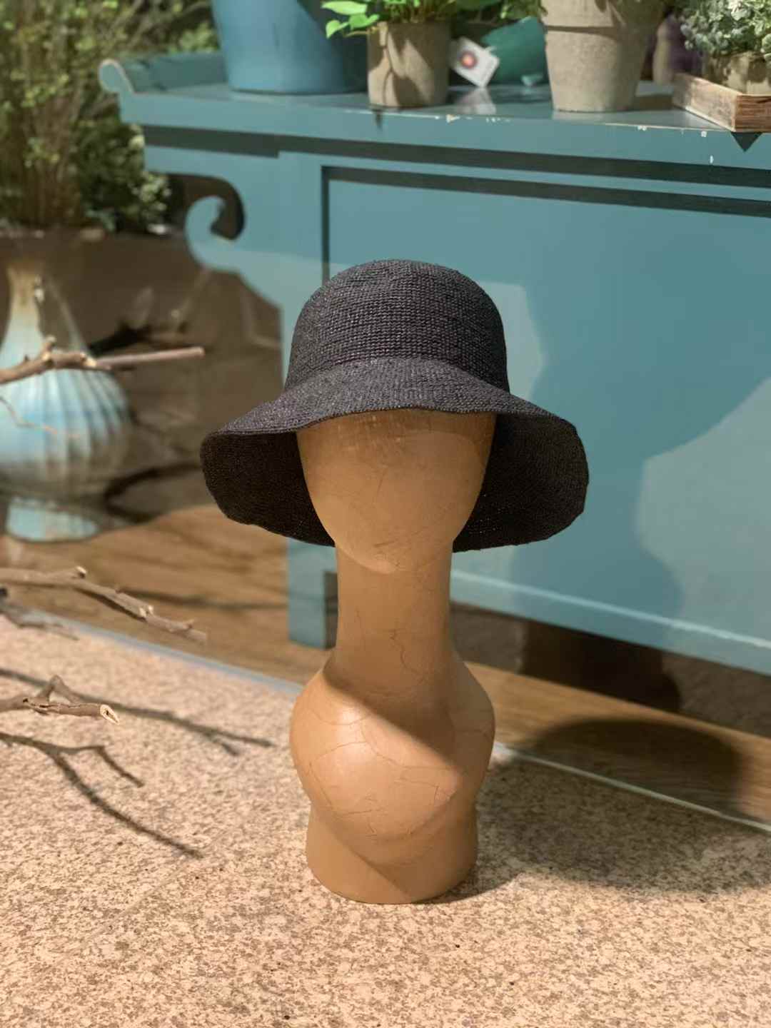 a black color straw hat on a wooden model, using natural raffia straw to hand crochet in plain stitches, very tight tension bucket hat style, and design for women