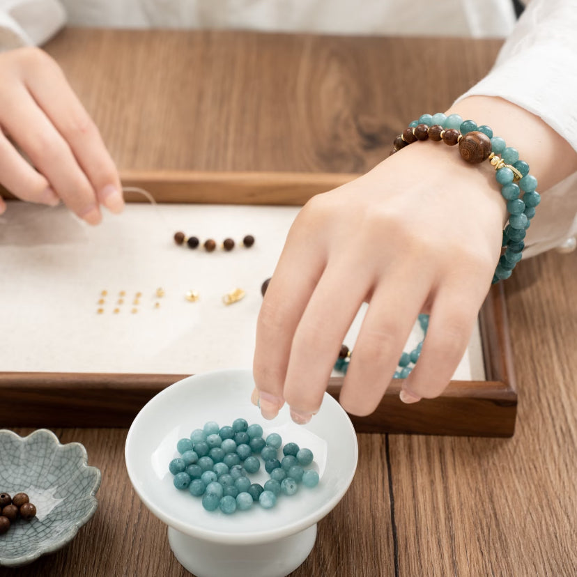 A women wearing a double wrap Chalcedony and sandalwood bracelet, she is making the bracelet, combines calming energy with the elegance of timeless Chinese design.