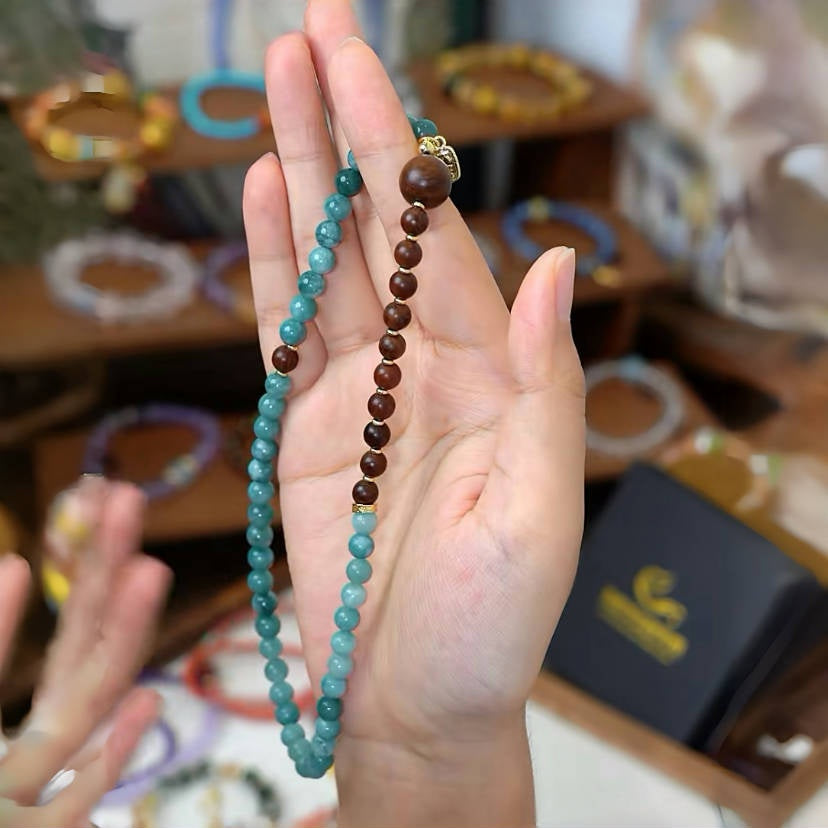 a hand holding a blue chalcedony and golden sandalwood beads bracelet, This handcrafted chalcedony & sandalwood bracelet channels peace and strength. Inspired by Chinese art—ideal as a unique spiritual gift.