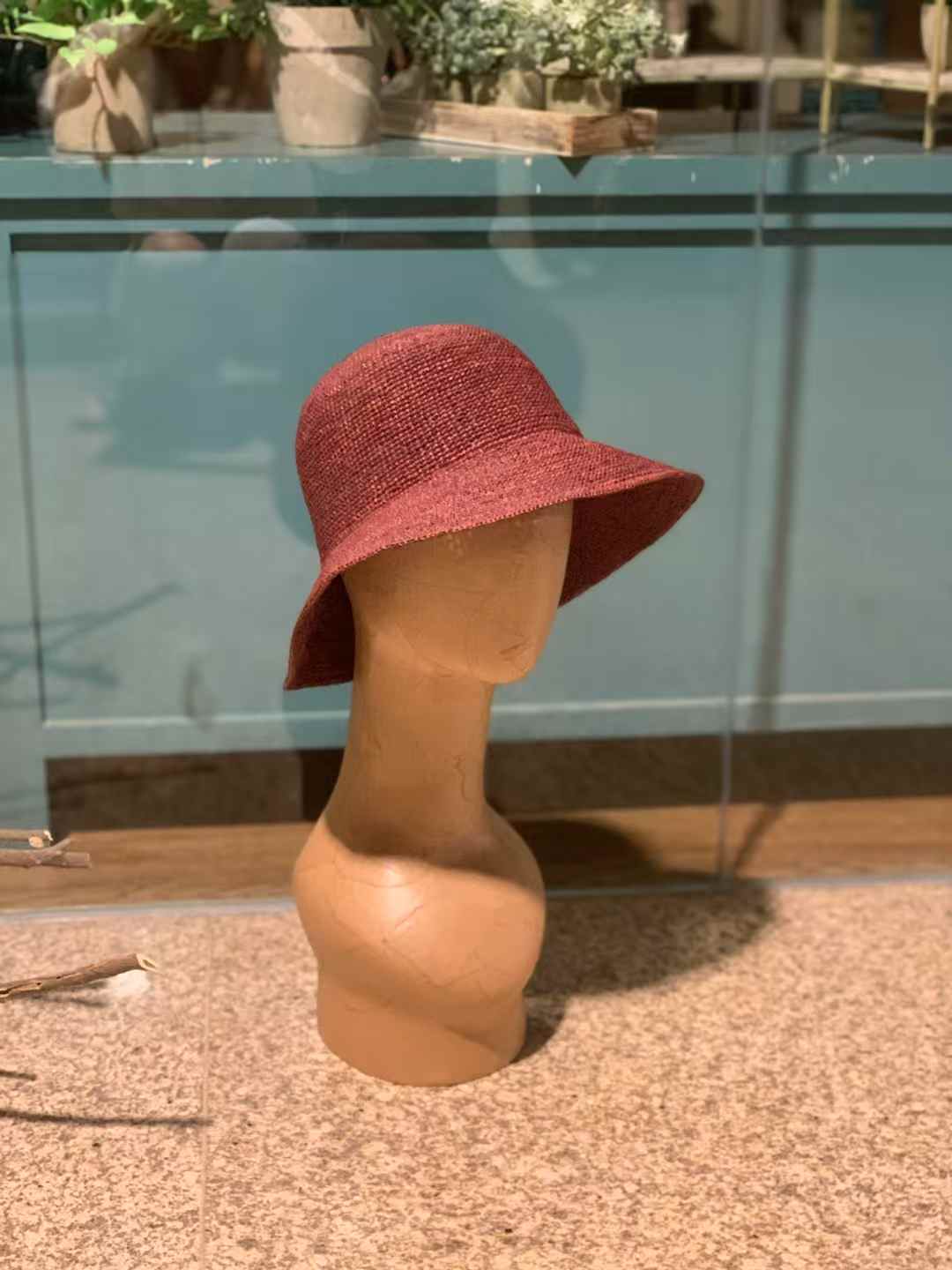 a red-wine color hat on a wooden model, using natural raffia straw to hand crochet in plain stitches, very tight tension bucket hat style, and design for women