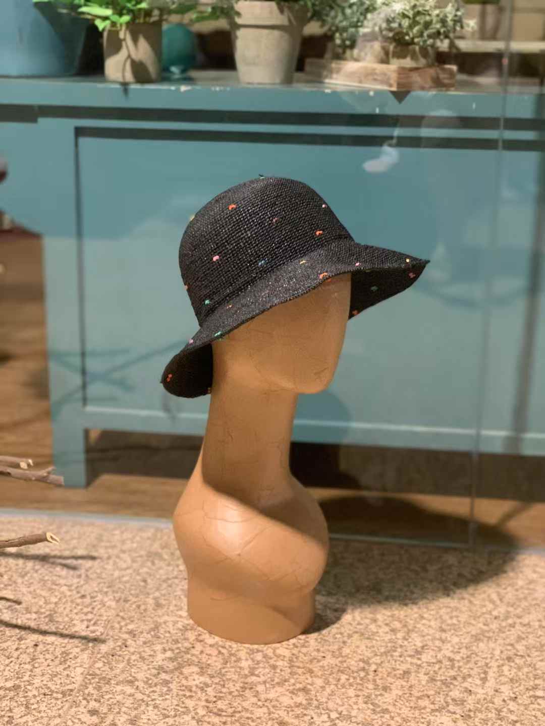 Black color raffia straw hat with wide brim and colorful speckles, hand-crocheted sun hat displayed on mannequin in rustic setting