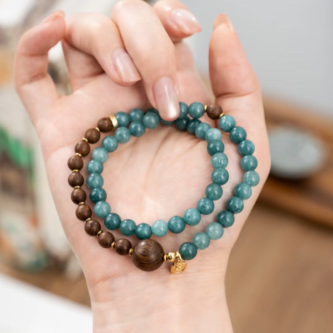a hand holding a double wrap bracelet with turquoise blue chalcedony and golden sandalwood beads, the design of this bracelet is inspired by Traditional Chinese art