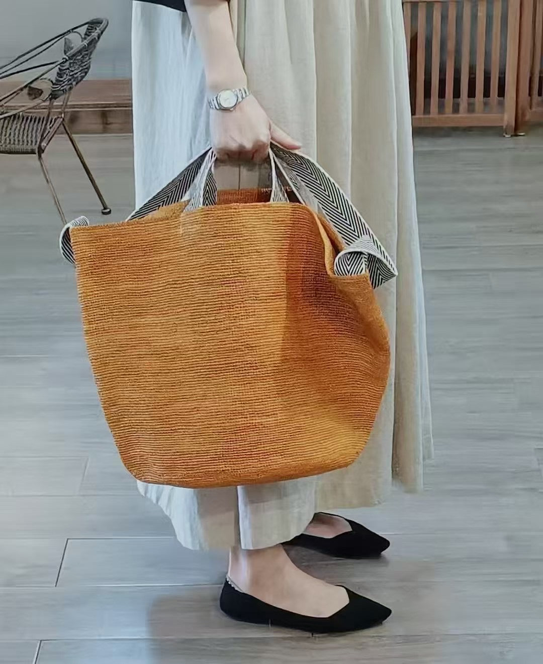 a website banner with a women holding an orange color raffia bag in hand, the raffia bag is a plain pattern solid color large tote in handmade, with a long herringbone cotton strap for crossbody wearing and 2 short handles for hand carry.