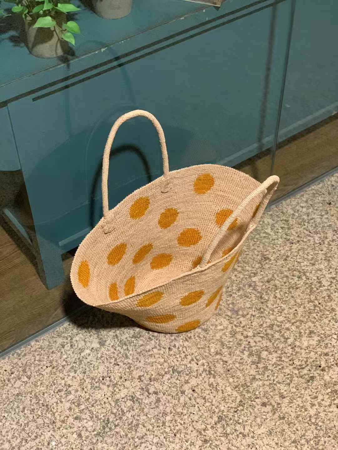 a wide opening vision of a Hand-crocheted raffia bag with natural base, and yellow polka dots all around the body, wide trapezoid shape with round bottom and raffia handles.