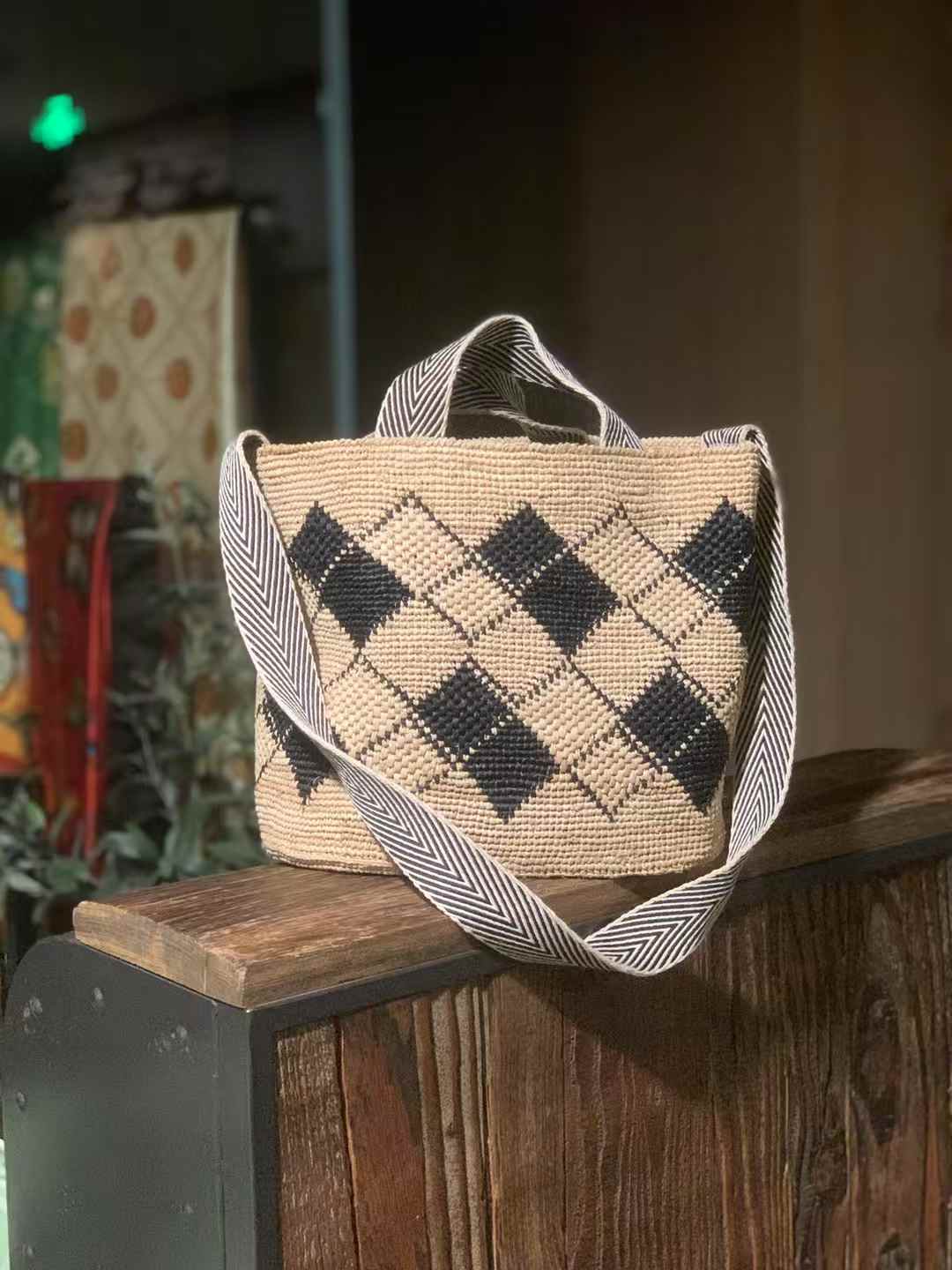 Straw Crossbody Bag in black diamond pattern, wide opening,  Features a wide, black-and-white striped cotton strap for easy crossbody or shoulder wear